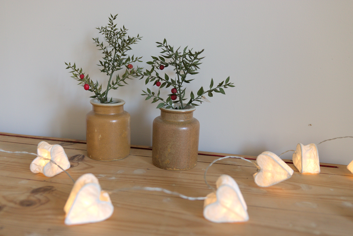 Anciens pots à moutarde marron vintage avec des branches de houx. Guirlande de coeur lumineuse sur un meuble en bois brut