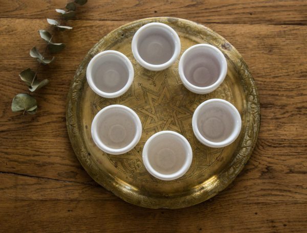 Petits pots en terre cuite émaillés en blanc artisanalement sur un plateau en bronze marocain avec une étoile sur une table en bois et avec de l'eucalyptus