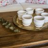 Petits pots en terre cuite émaillés en blanc artisanalement sur un plateau en bronze marocain sur une table en bois et avec de l'eucalyptus