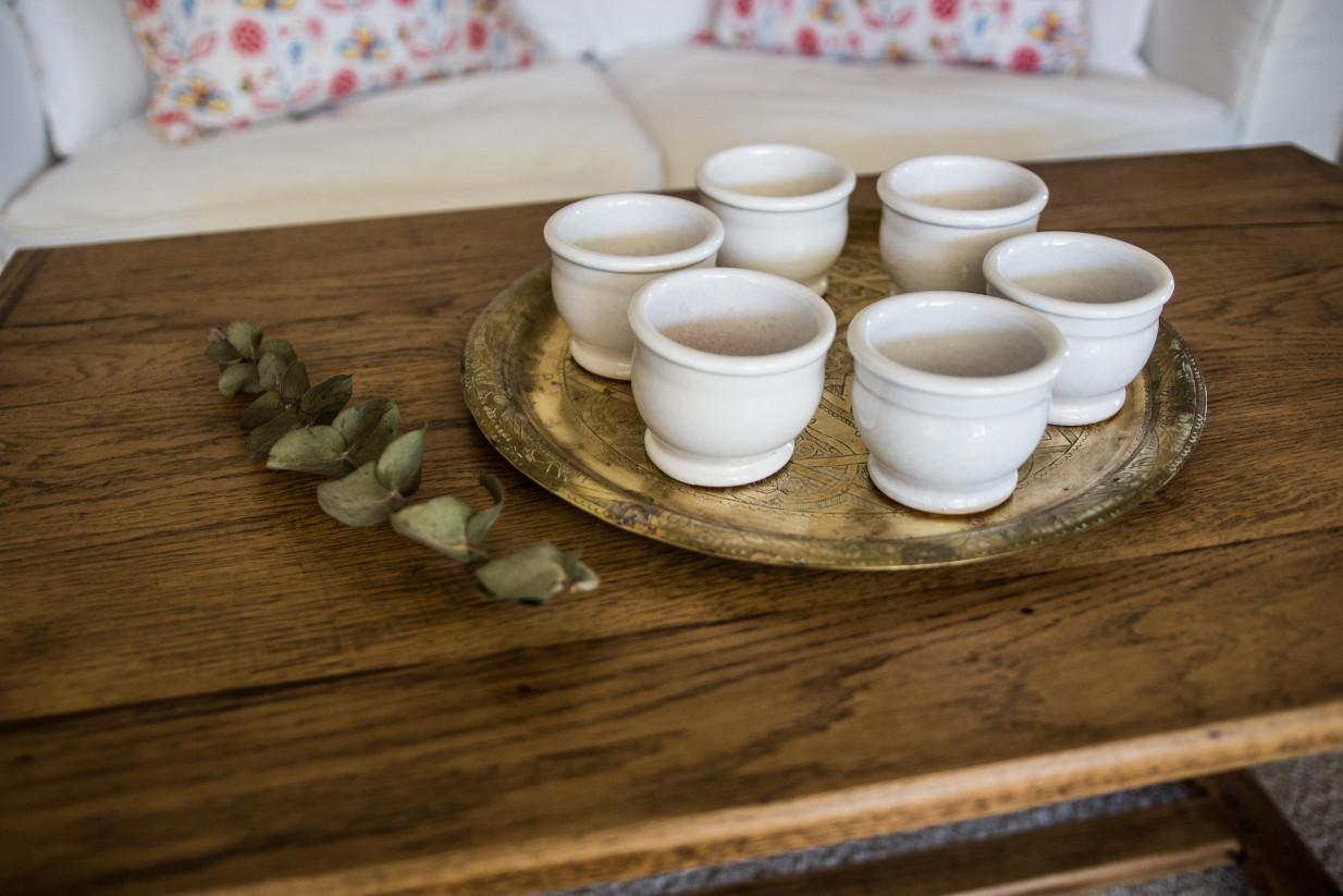 Petits pots en terre cuite émaillés en blanc artisanalement sur un plateau en bronze marocain sur une table en bois et avec de l'eucalyptus