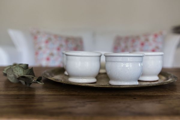 Petits pots en terre cuite émaillés en blanc artisanalement sur un plateau en bronze marocain sur une table en bois et avec de l'eucalyptus