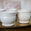 Petits pots en terre cuite émaillés en blanc artisanalement sur un plateau en bronze marocain sur une table en bois et avec de l'eucalyptus