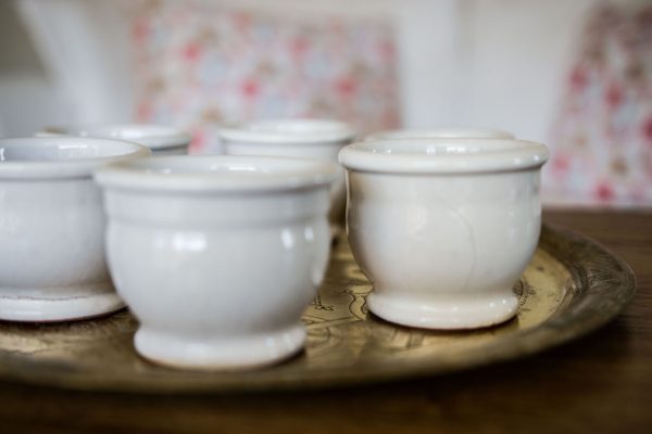 Petits pots en terre cuite émaillés en blanc artisanalement sur un plateau en bronze marocain sur une table en bois et avec de l'eucalyptus