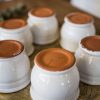 Petits pots en terre cuite émaillés en blanc artisanalement sur un plateau en bronze marocain sur une table en bois et avec de l'eucalyptus