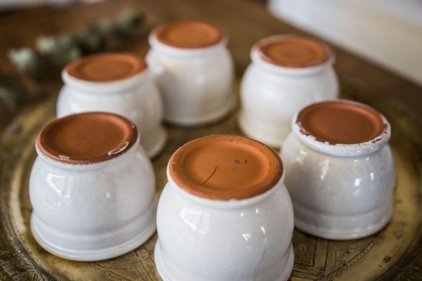 Petits pots en terre cuite émaillés en blanc artisanalement sur un plateau en bronze marocain sur une table en bois et avec de l'eucalyptus