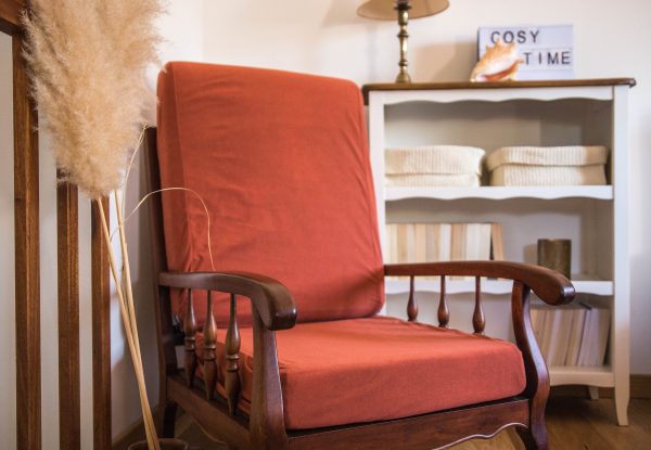 Fauteuil de couleur terracotta vintage en bois foncé. Présenté avec des herbes de la pampa, un meuble en bois blanc et des livres. Cosy time