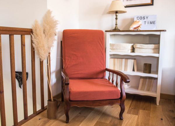 Fauteuil de couleur terracotta vintage en bois foncé. Présenté avec des herbes de la pampa, un meuble en bois blanc et des livres. Cosy time