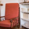 Fauteuil de couleur terracotta vintage en bois foncé. Présenté avec des herbes de la pampa, un meuble en bois blanc et des livres. Cosy time