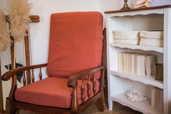 Fauteuil de couleur terracotta vintage en bois foncé. Présenté avec des herbes de la pampa, un meuble en bois blanc et des livres. Cosy time