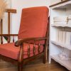 Fauteuil de couleur terracotta vintage en bois foncé. Présenté avec des herbes de la pampa, un meuble en bois blanc et des livres. Cosy time