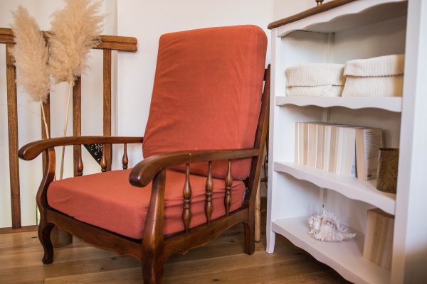 Fauteuil de couleur terracotta vintage en bois foncé. Présenté avec des herbes de la pampa, un meuble en bois blanc et des livres. Cosy time