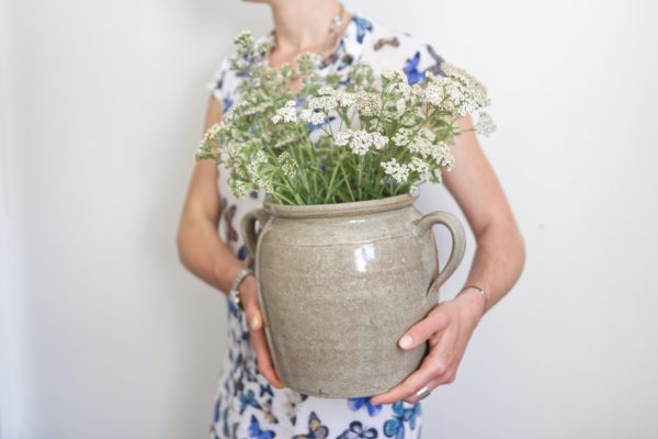 Pot en grès ancien avec des anses servant de vase pour des fleurs sauvages blanches. Porté sur la hanche. Robe fleurie printanière