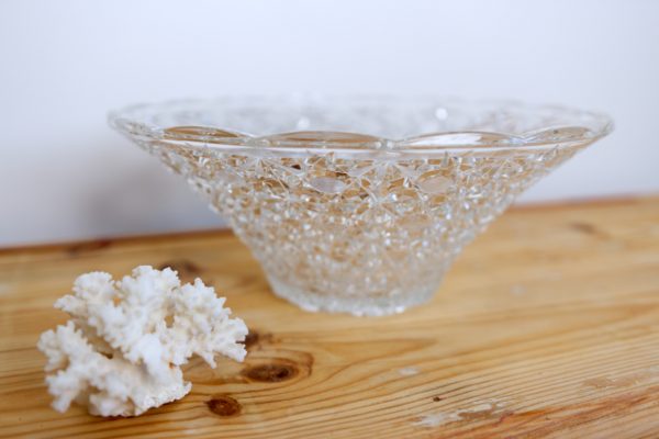 Vase évasé en verre travaillés avec des motifs sur une table en bois brut et avec un corail blanc