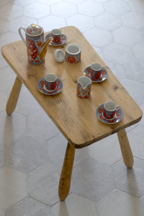 Service à café japonais rouge et doré avec un pot à lait six tasses une théière sur une table en bois brut clair et carrelage gris hexagonal