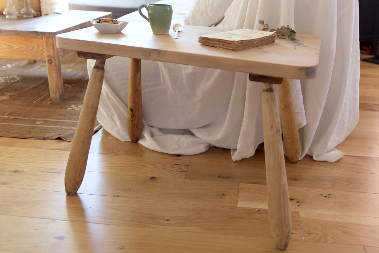 Table basse en bois clair asymétrique en bout de canapé. Style vintage maison avec parquet tapis kilim et canapé en lin blanc