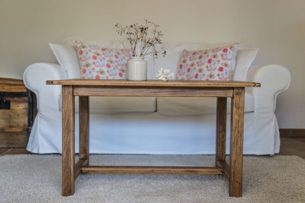 Table en bois brut rénovée vintage poncée et vernie. Canapé blanc, malle ancienne, corail et fleurs séchées dans un pot à moutarde en grès ancien