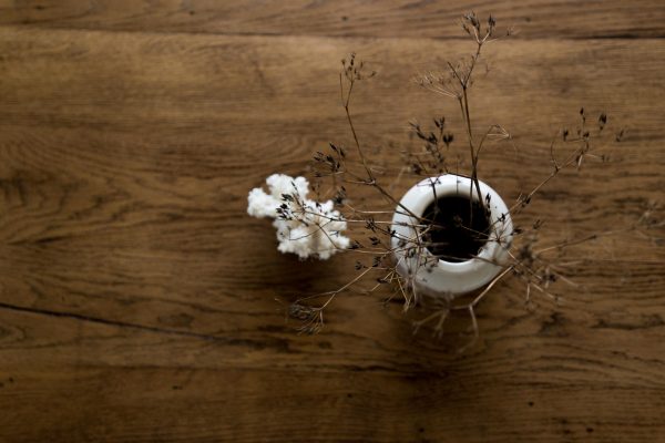 Table en bois brut rénovée vintage poncée et vernie. Canapé blanc, malle ancienne, corail et fleurs séchées dans un pot à moutarde